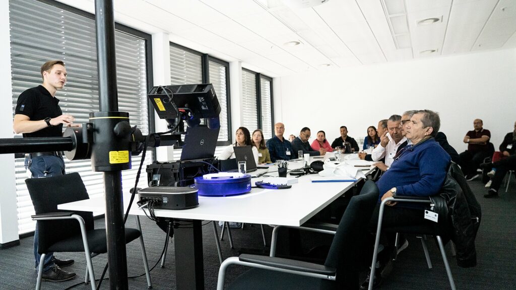 Eine Gruppe von Menschen sitzt in einem Besprechungsraum. Ein Mann hält vor ihr eine Präsentation.