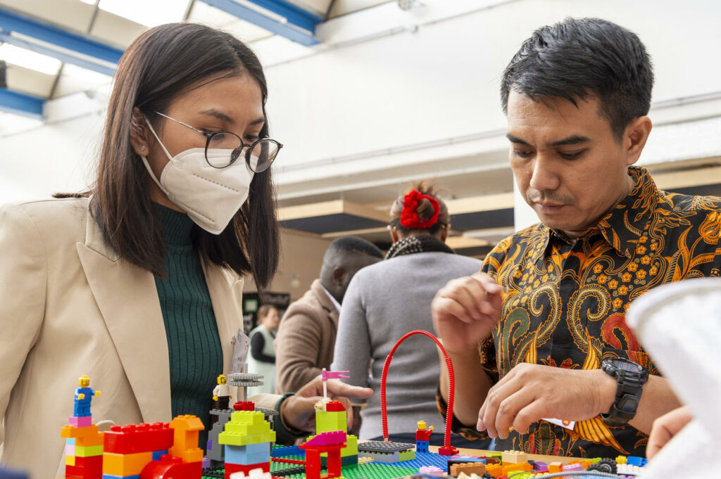 A group of men and women stand in front of a table with Lego bricks