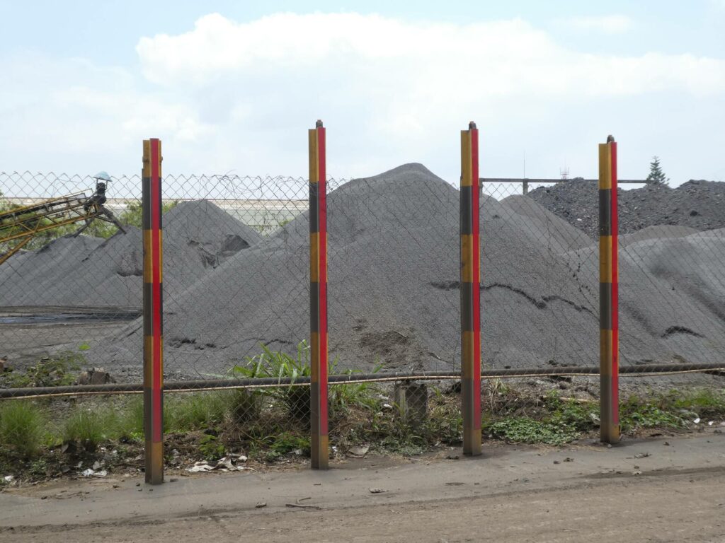 A wire mesh fence with mountains of black slag behind it.