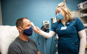 A nurse taking the temperature of a patient with a forehead infrared thermometer, both are wearing face masks.