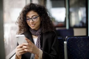 Smiling young woman traveling by bus and using smart phone